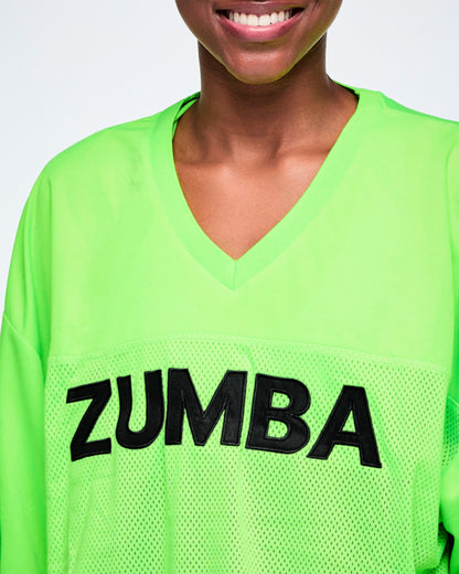 Close-up of a female model wearing a bright green V-neck mesh jersey with large black 'ZUMBA' lettering across the chest.